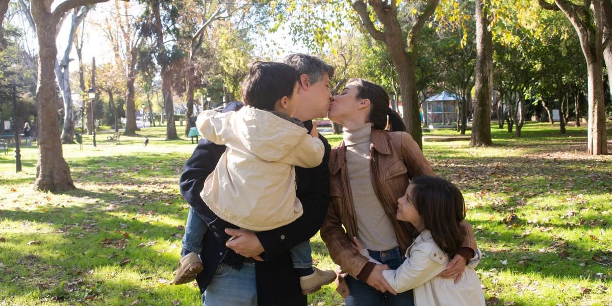 A joyful family sharing a tender moment in a sunny park setting.