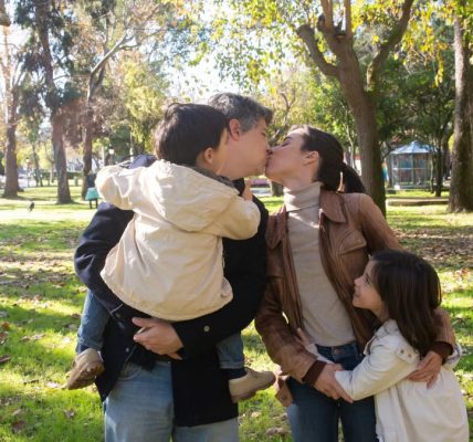 A joyful family sharing a tender moment in a sunny park setting.
